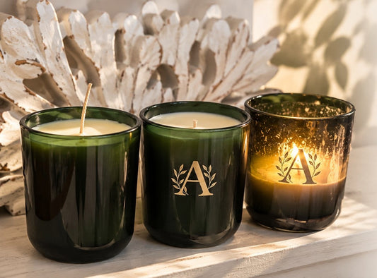 Three green A Candle Collection candles at different burn stages on a white wooden surface